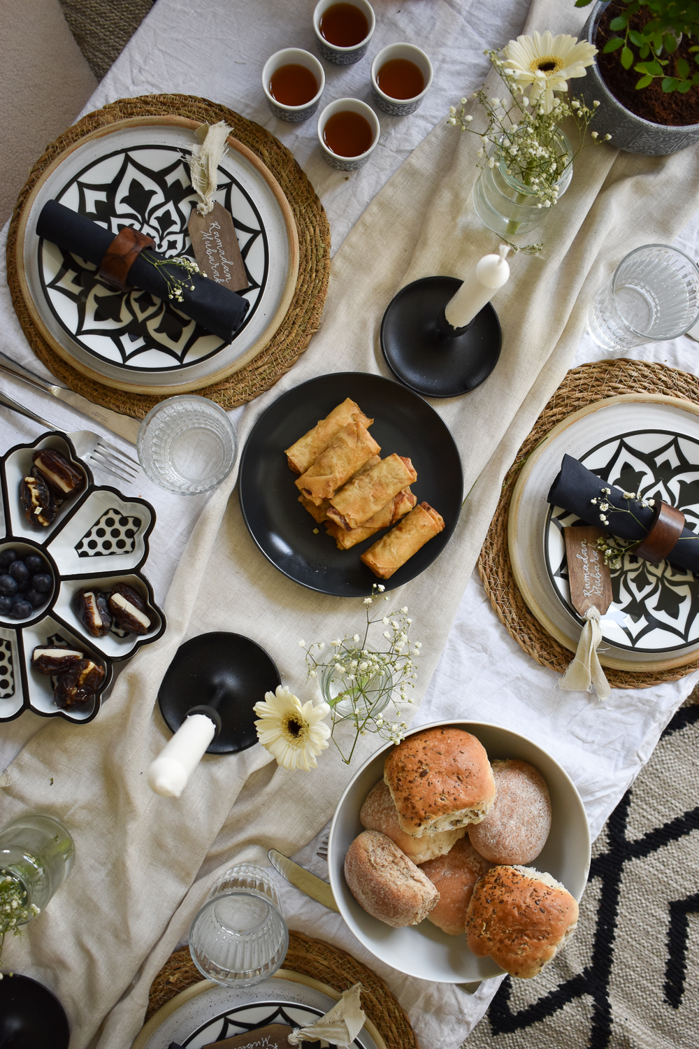 Overhead view of Ramadan tablescape with place settings, food, and centerpiece vignette on white linen tablecloth