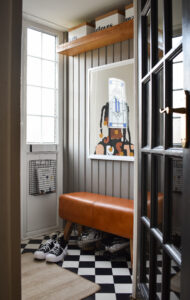 A small porch areas with a faux leather bench and a large art frame of a young girl with hair in braids