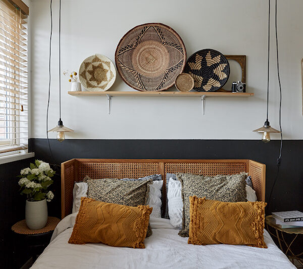 a forward view of the bed with the rattan headboard and wooden shelf above the bed. there are two hanging lights on pendant wires. 