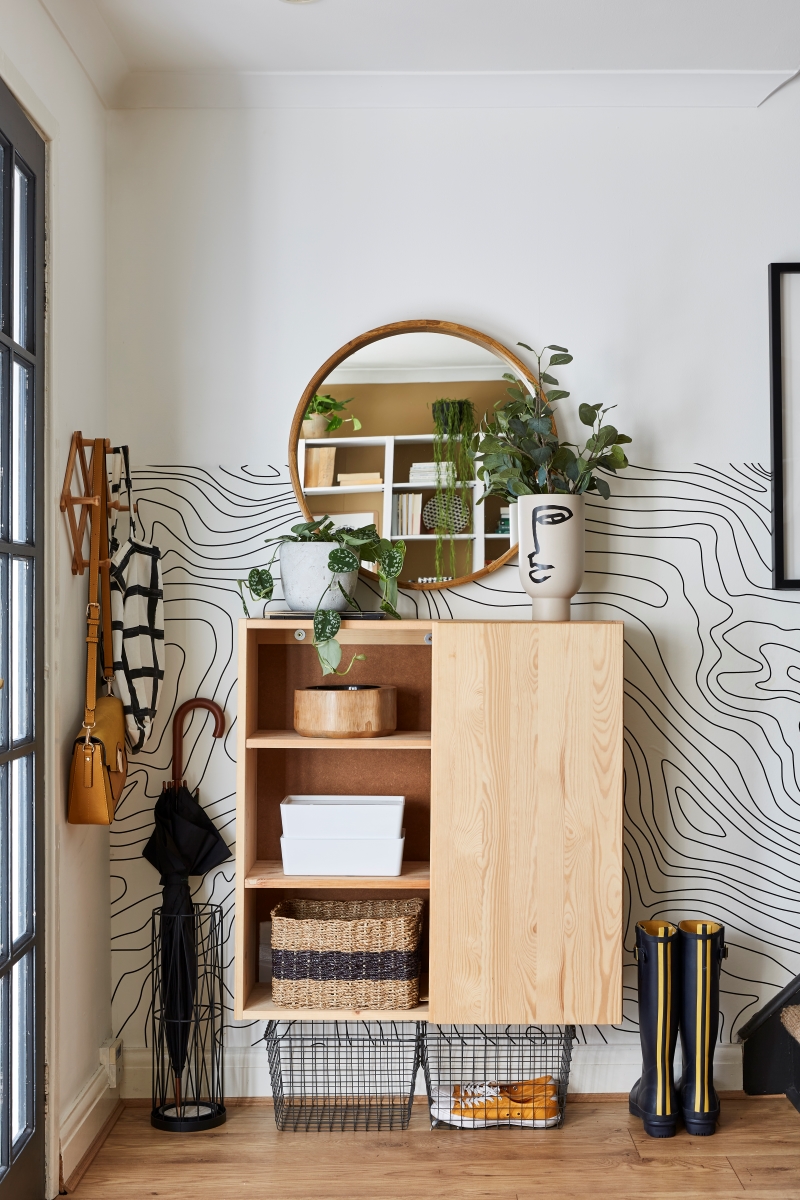 Entryway with Ikea Ivar cabinet hack using one door on the left and open shelves on the right, graphic black and white wallpaper halfway up the wall next to stairway.