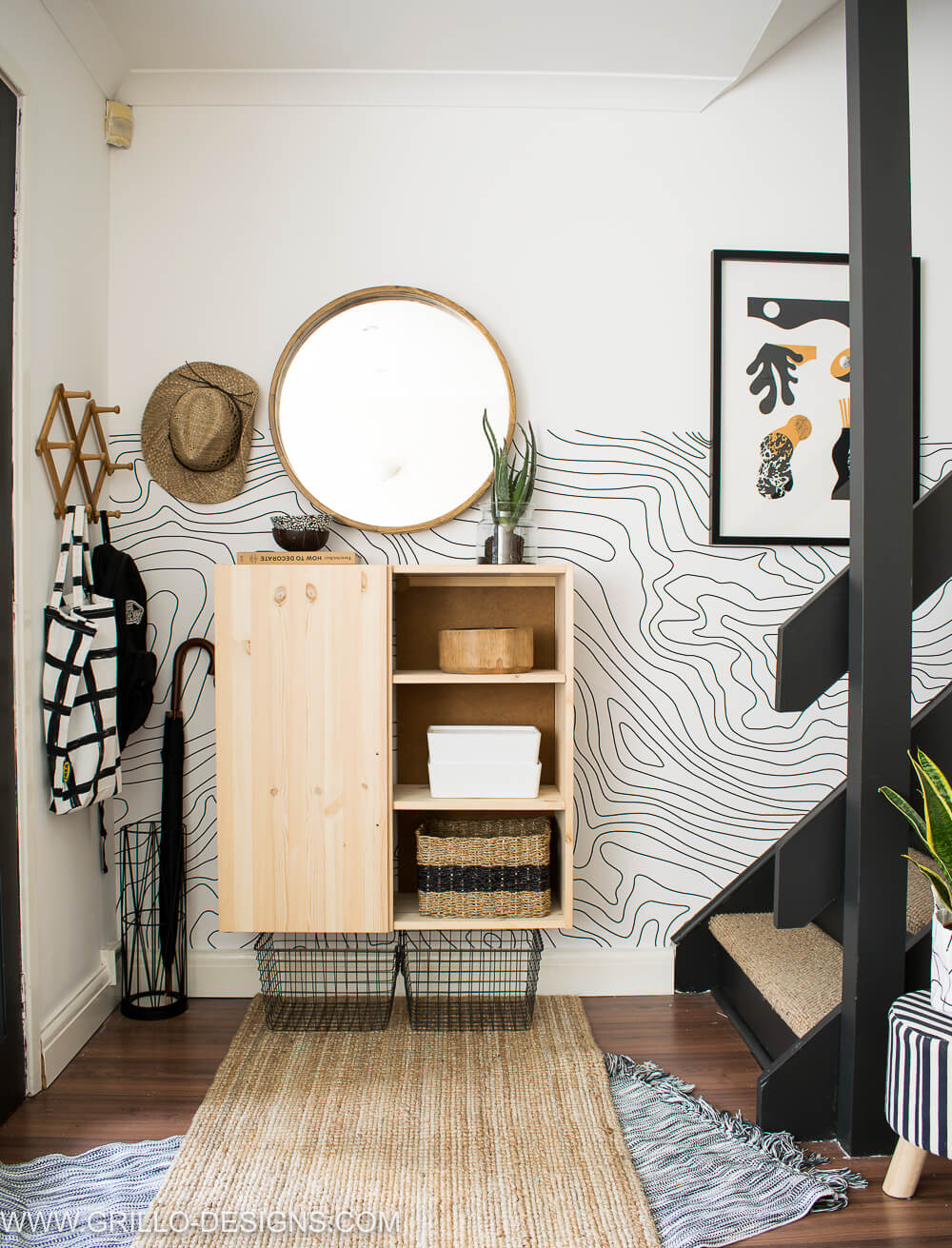 Entryway with Ikea Ivar hack using one door on the right and open shelves on the left, graphic black and white wallpaper halfway up the wall next to stairs.