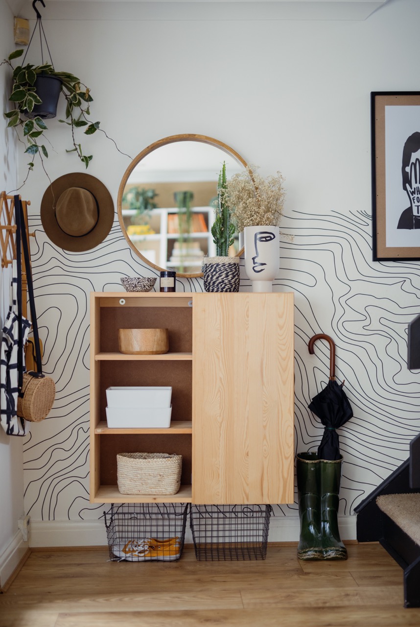 Entryway with Ikea Ivar cabinet hack using one door on the left and open shelves on the right, graphic black and white wallpaper halfway up the wall next to stairway.