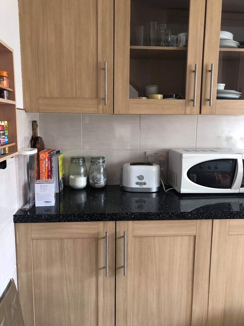 Wood-fronted kitchen with upper and lower cabinets and a black worktop.