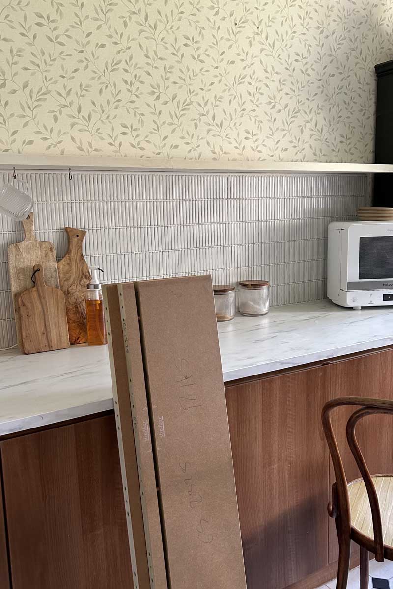 Floating shelves waiting to be installed above wooden kitchen units, a faux marble worktop and a tiled splashback.